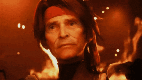 a man wearing a red headband stands in front of flames