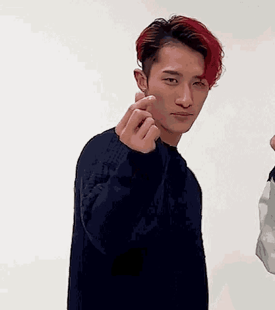 a man with red hair is wearing a black sweater and making a heart with his hands .