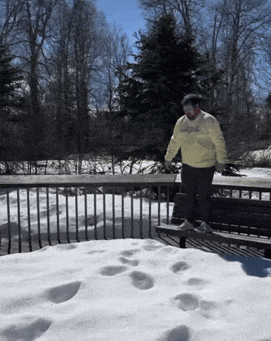 a man wearing a yellow sweatshirt that says university of michigan stands on a snowy deck