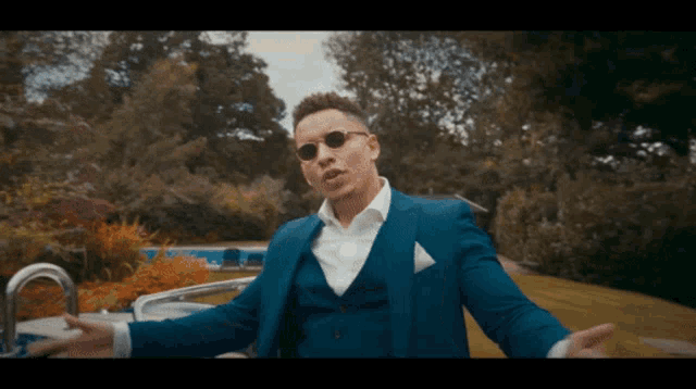 a man in a blue suit and sunglasses is standing in front of a pool
