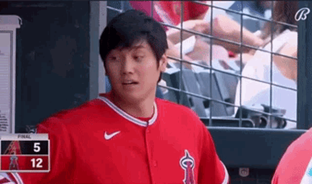 a baseball player in a red uniform is standing in a dugout during a game .