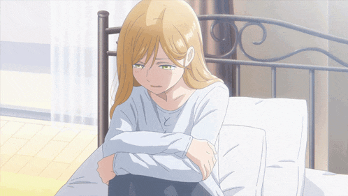 a blonde anime girl is sitting on a bed with her arms crossed