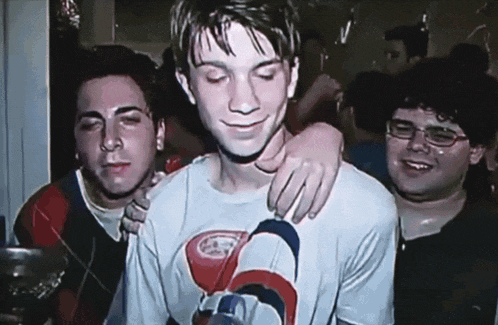 a man wearing a shirt with the letter g on it is being hugged by two other men
