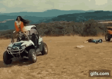 a woman is riding a buggy on a dirt road while a man is laying on the ground .