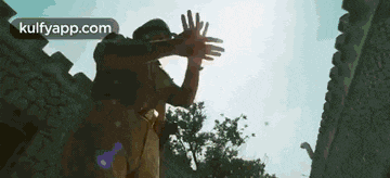 a man is standing in front of a stone wall with his hands up .