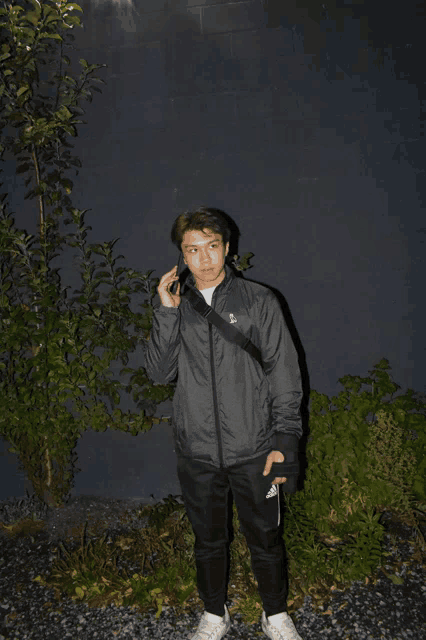 a man wearing a grey adidas jacket is standing in front of a dark wall