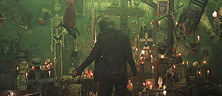a man in a black jacket stands in a room with candles and skeletons