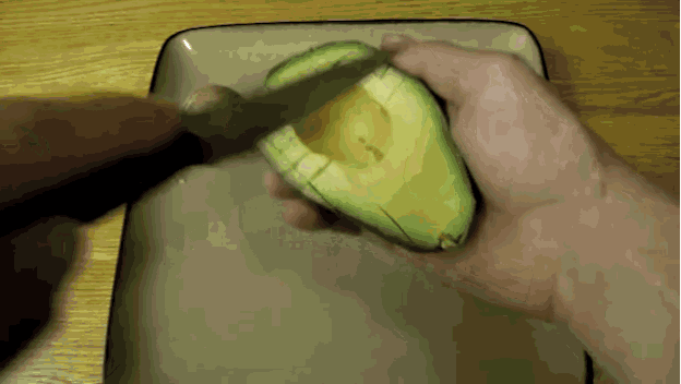 a person cutting an avocado with a knife on a plate
