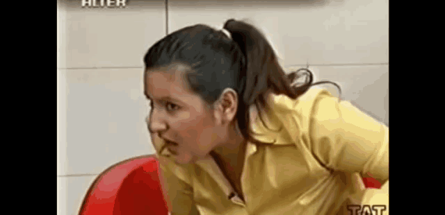 a woman in a yellow shirt is sitting on a red chair in front of a sign that says tat
