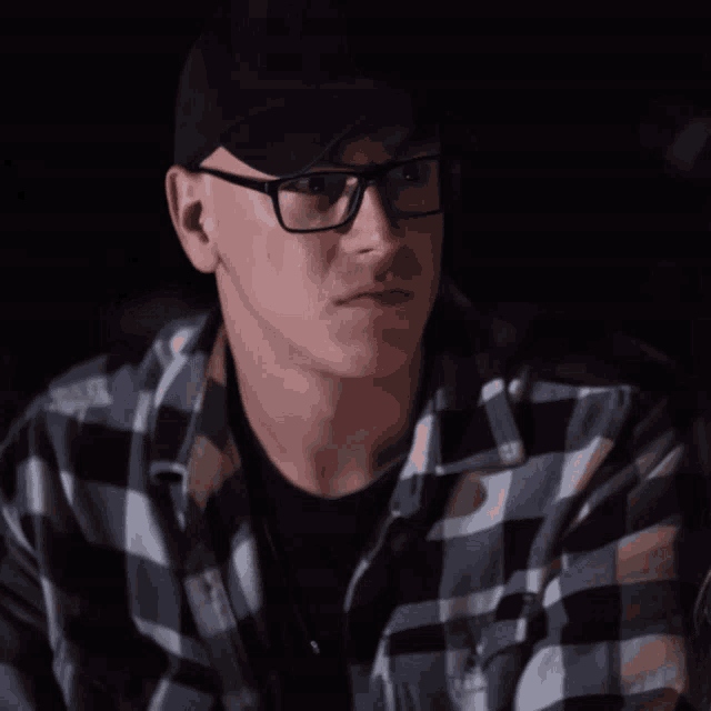 a man wearing glasses and a plaid shirt looks at the camera