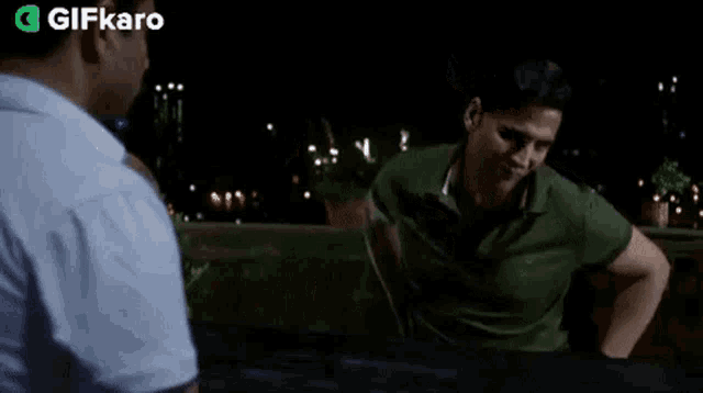 a man in a green shirt is holding a gun and pointing at another man .