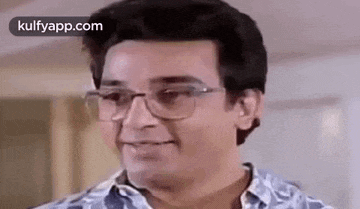 a man wearing glasses and a blue shirt is smiling and looking at the camera .