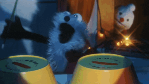 elmo from sesame street is playing drums in front of two yellow cups