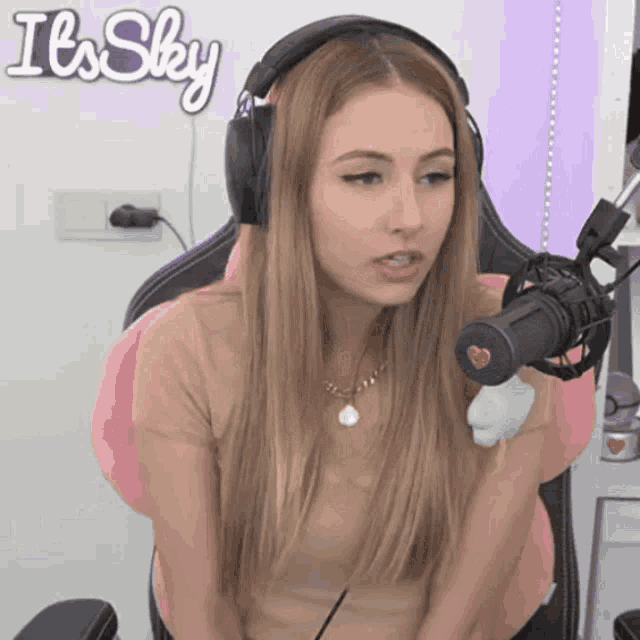 a woman wearing headphones is sitting in front of a microphone with the words it 's sky behind her