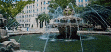 a fountain with a building in the background is surrounded by trees