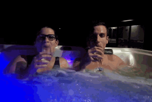 a man and a woman are in a hot tub drinking wine