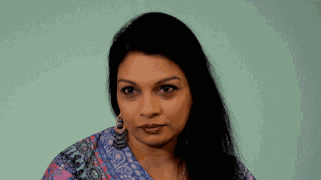 a woman wearing earrings and a floral shirt looks at the camera