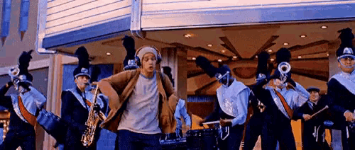 a man wearing headphones is dancing in front of a marching band playing instruments .