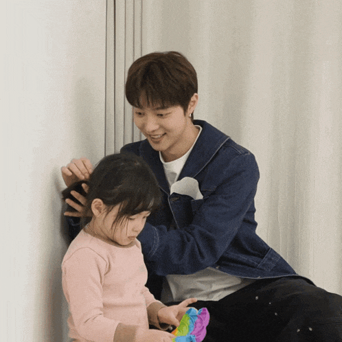 a man is brushing a little girl 's hair while holding a toy