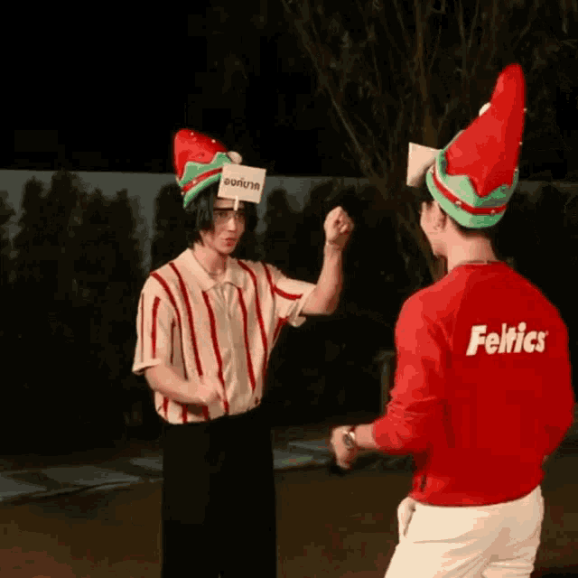 a man wearing a red feltics shirt stands next to another man wearing a santa hat
