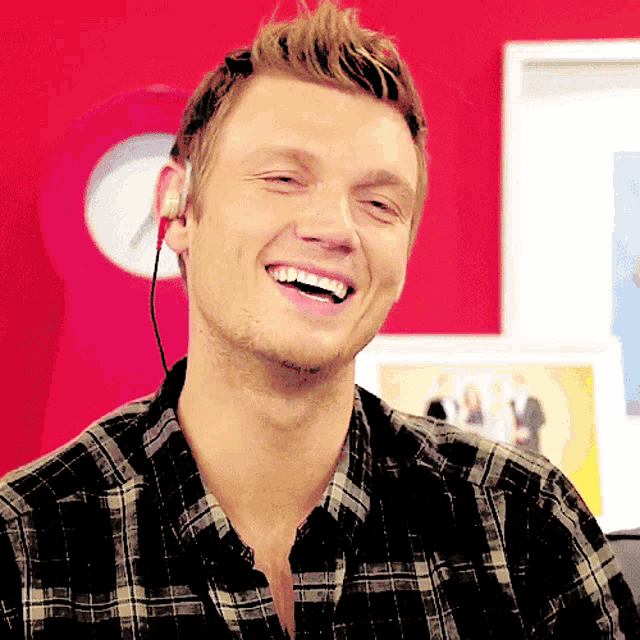 a man wearing a plaid shirt and ear buds smiles