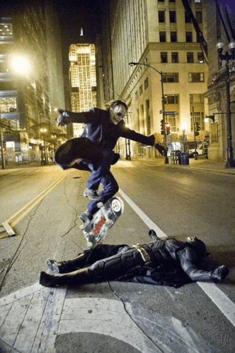 a man in a joker mask is riding a skateboard over a batman laying on the ground