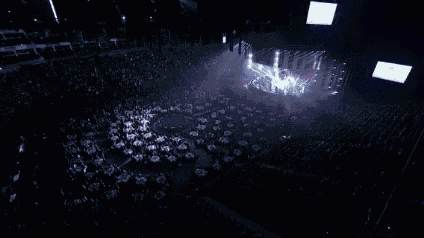 a group of people are sitting in a dark room watching a concert with a lot of lights on the stage .