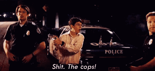 a man is being arrested by police officers in front of a police car and says shit the cops .