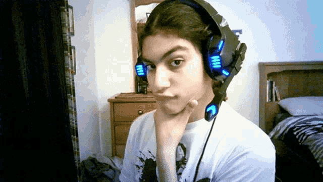 a young man wearing headphones looks at the camera with his hand on his chin