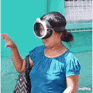 a woman wearing a blue shirt and goggles is standing in front of a green building .