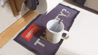 a coffee mug is sitting on a mat that says " thwaites "