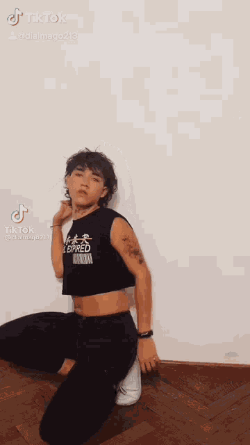 a young man wearing a crop top and black pants is kneeling down on the floor .