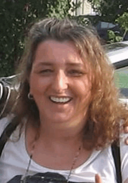 a woman with curly hair is smiling for the camera while wearing a white shirt and a backpack .