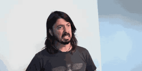 a man with long hair and a beard is wearing a black t-shirt and making a funny face .