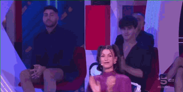 a group of people are sitting on a couch and applauding a woman in a purple top .