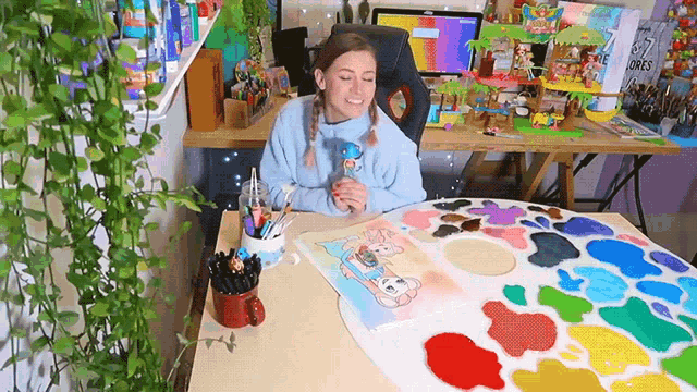 a woman is sitting at a table with a palette of paint and a painting on it