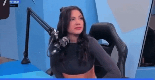 a woman is sitting in a chair in front of a microphone and looking at the camera .