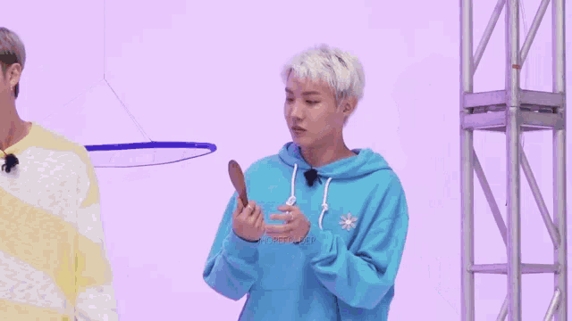 a man in a blue hoodie is holding a wooden spoon in his hand and making a funny face .