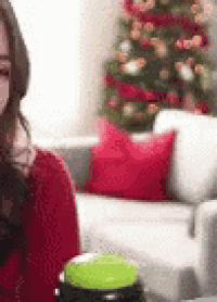 a woman in a red sweater is sitting on a couch holding a green button .