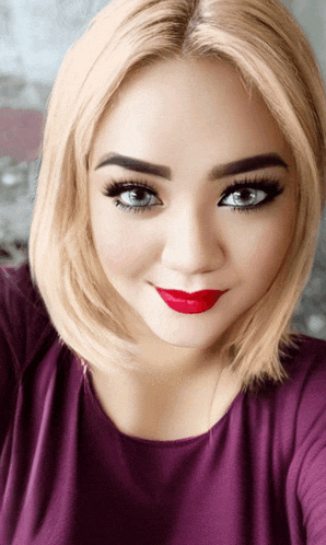 a woman wearing a purple shirt and red lipstick takes a selfie