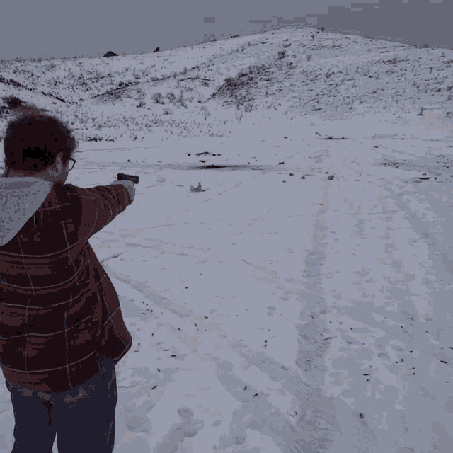 a man in a plaid shirt is pointing a gun at a fireball in the snow