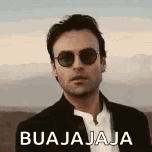 a man wearing sunglasses and a suit is standing in a desert .
