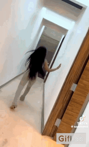 a woman with long black hair is standing in a hallway holding a door open .