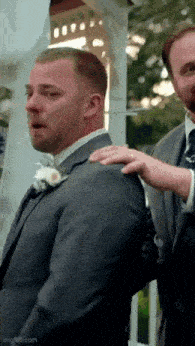 a man in a suit is crying while another man holds his shoulder .