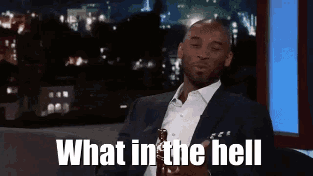 a man in a suit is sitting in front of a screen with the words what in the hell written on it .