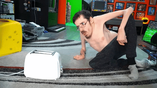 a shirtless man is kneeling down next to a toaster