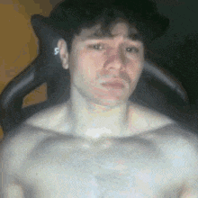 a man without a shirt is sitting in a chair and making a funny face .