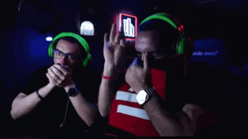 two men wearing green headphones are playing a video game in a dark room