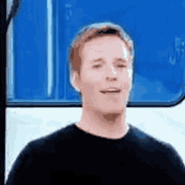 a man in a black shirt is standing in front of a blue and white vehicle .