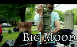 a man in a blue shirt is standing next to a motorcycle with the words big mood written above him .